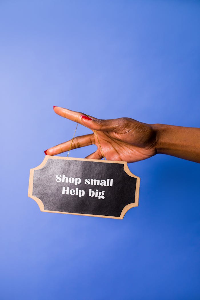 A hand holding a sign reading 'Shop small, Help big' against a blue background.